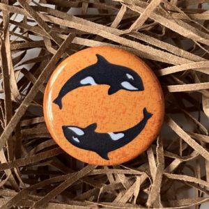 1" button of two orca whales against a mottled orange background