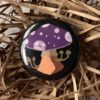 black button with a purple mushroom in the center