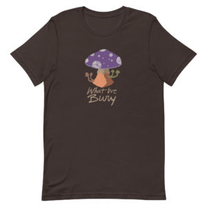 Brown short-sleeve t-shirt featuring a purple toadstool mushroom with four smaller mushrooms budding from the stipe. Text underneath reads "What We Bury."